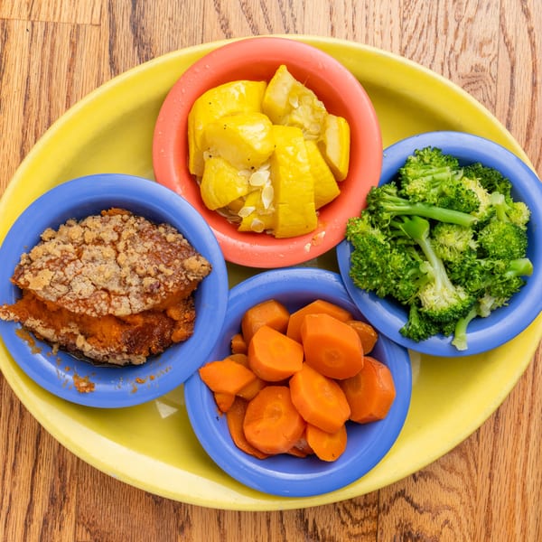 Southern side dishes: sweet potato casserole, squash, broccoli, and carrots on a yellow tray.