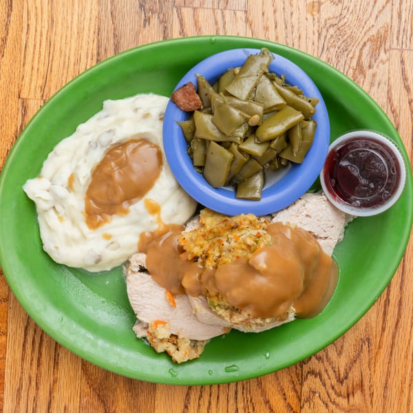 Southern-style turkey and dressing with mashed potatoes, green beans, and gravy on a green plate.