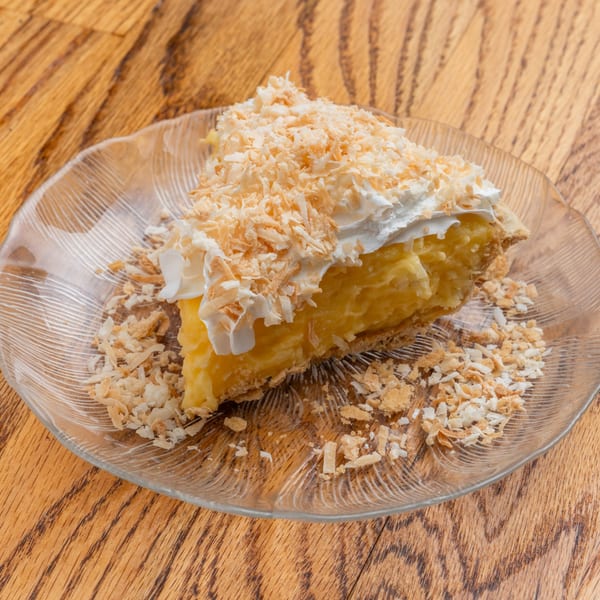 Slice of The String Bean's southern coconut cream pie with whipped topping and toasted coconut flakes.