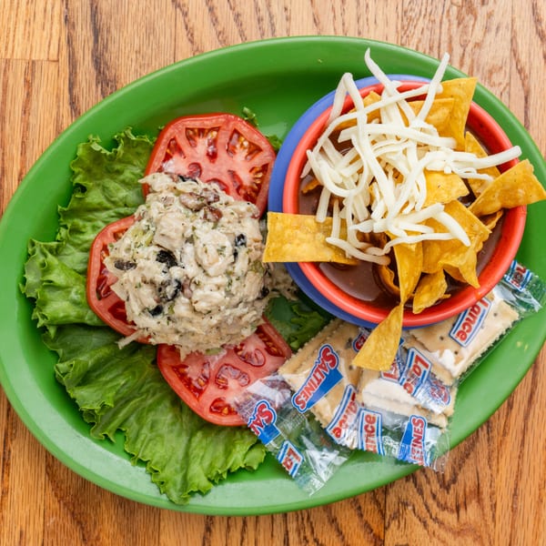 Southern chicken salad with sliced tomatoes, lettuce, chili, tortilla chips, and crackers on a green plate.