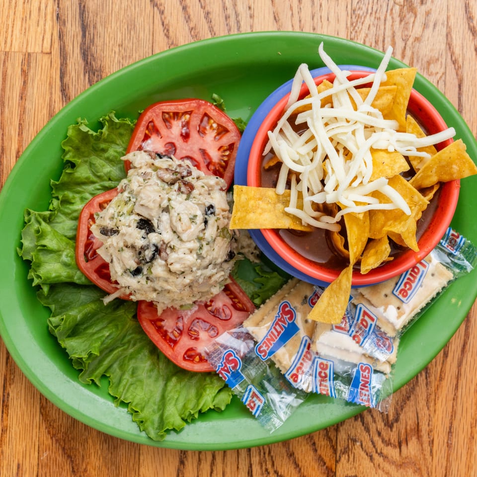 Southern chicken salad with sliced tomatoes, lettuce, chili, tortilla chips, and crackers on a green plate.