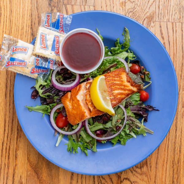 Grilled salmon salad with mixed greens, red onion, cherry tomatoes, lemon, dressing, and crackers.