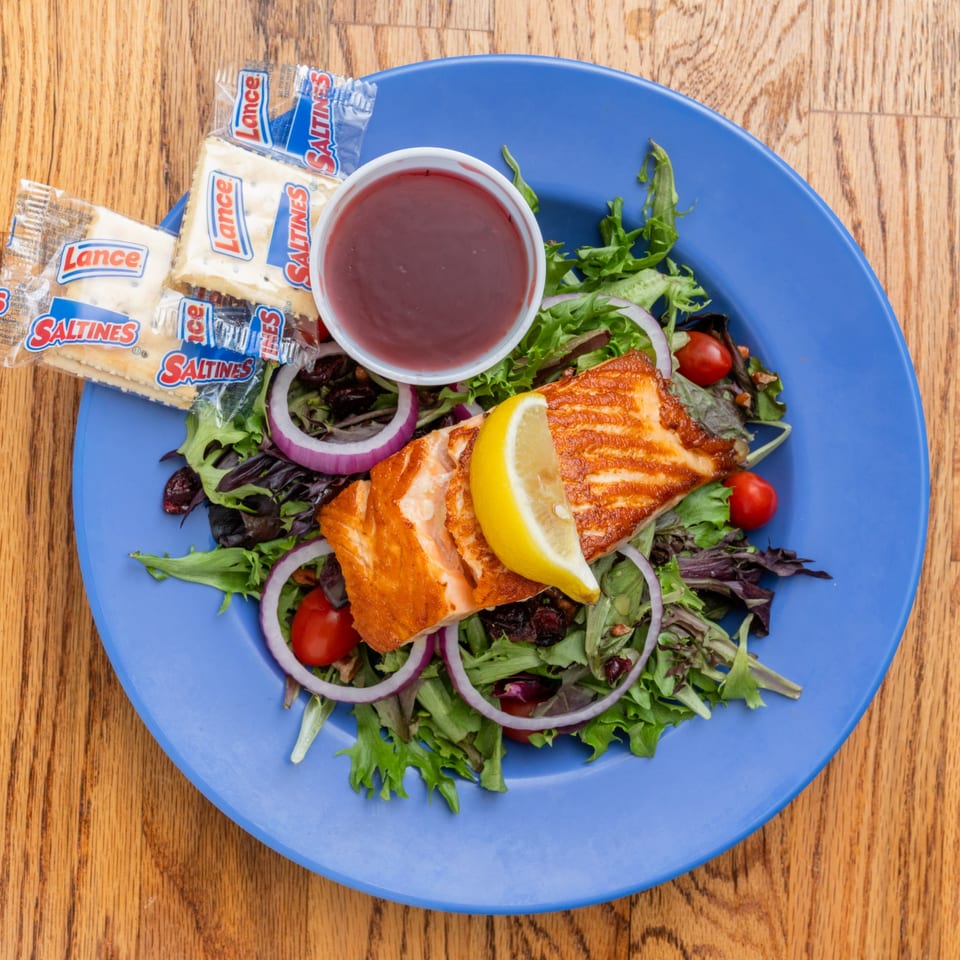 Grilled salmon salad with mixed greens, red onion, cherry tomatoes, lemon, dressing, and crackers.