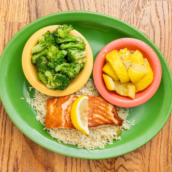 A Southern-style salmon fillet with a lemon wedge, rice, steamed broccoli, and yellow squash.