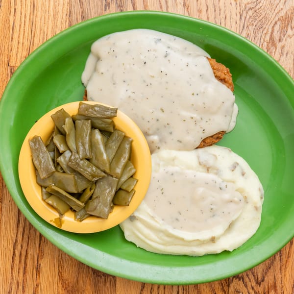 Southern chicken fried steak with gravy, mashed potatoes, and green beans on a green plate.