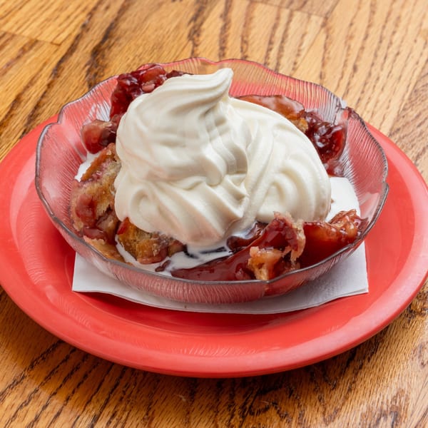 Southern cherry cobbler with a dollop of whipped cream, served in a clear bowl on a red plate.