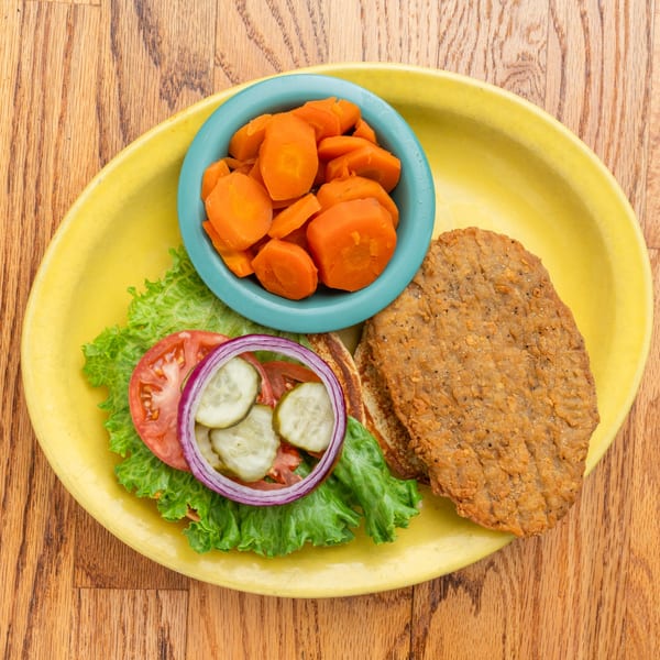 Southern fried steak with lettuce, tomato, onion, pickles, and a side of carrots.