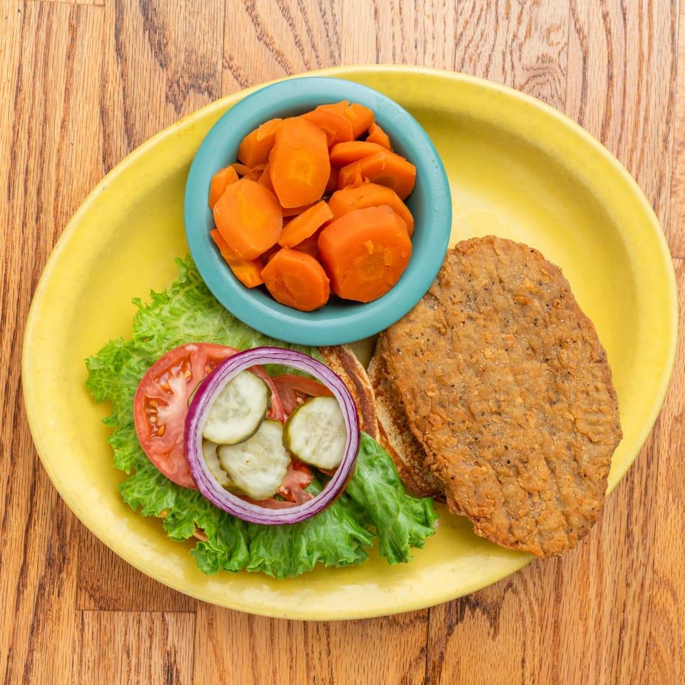 Southern fried steak with lettuce, tomato, onion, pickles, and a side of carrots.